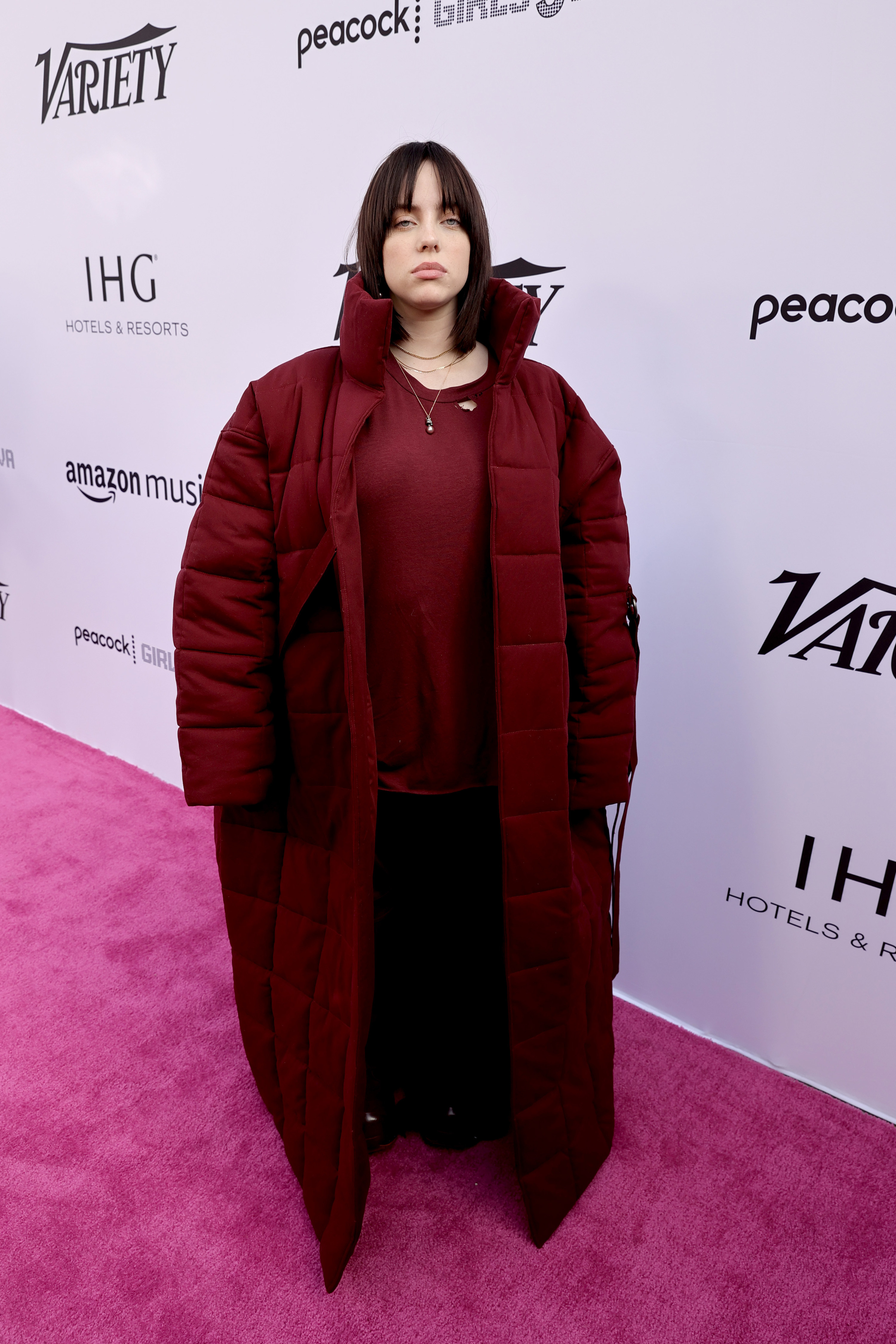 A brunette Billie on the red carpet in a long quilted burgundy coat