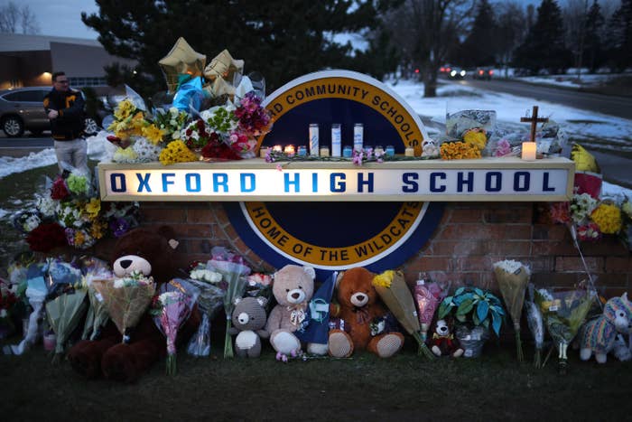 Stuffed animals and flowers are placed on the ground up against the Oxford High School brick sign