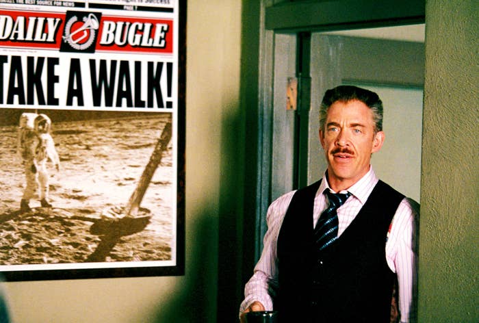J.K. as Jameson leaning against a doorframe next to a poster of the Daily Bugle