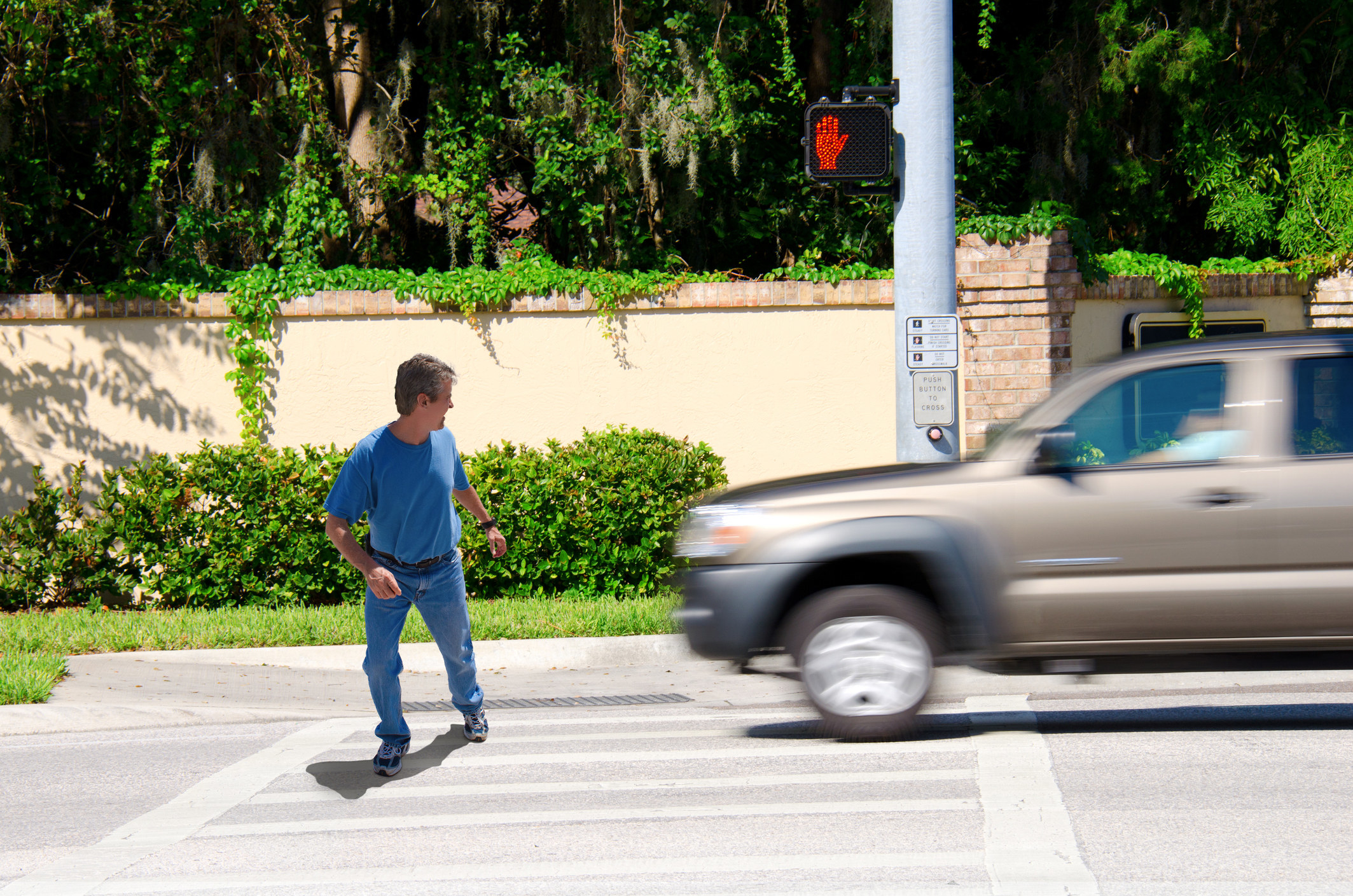 Man crossing the street at a crosswalk against a red light as a car goes by him