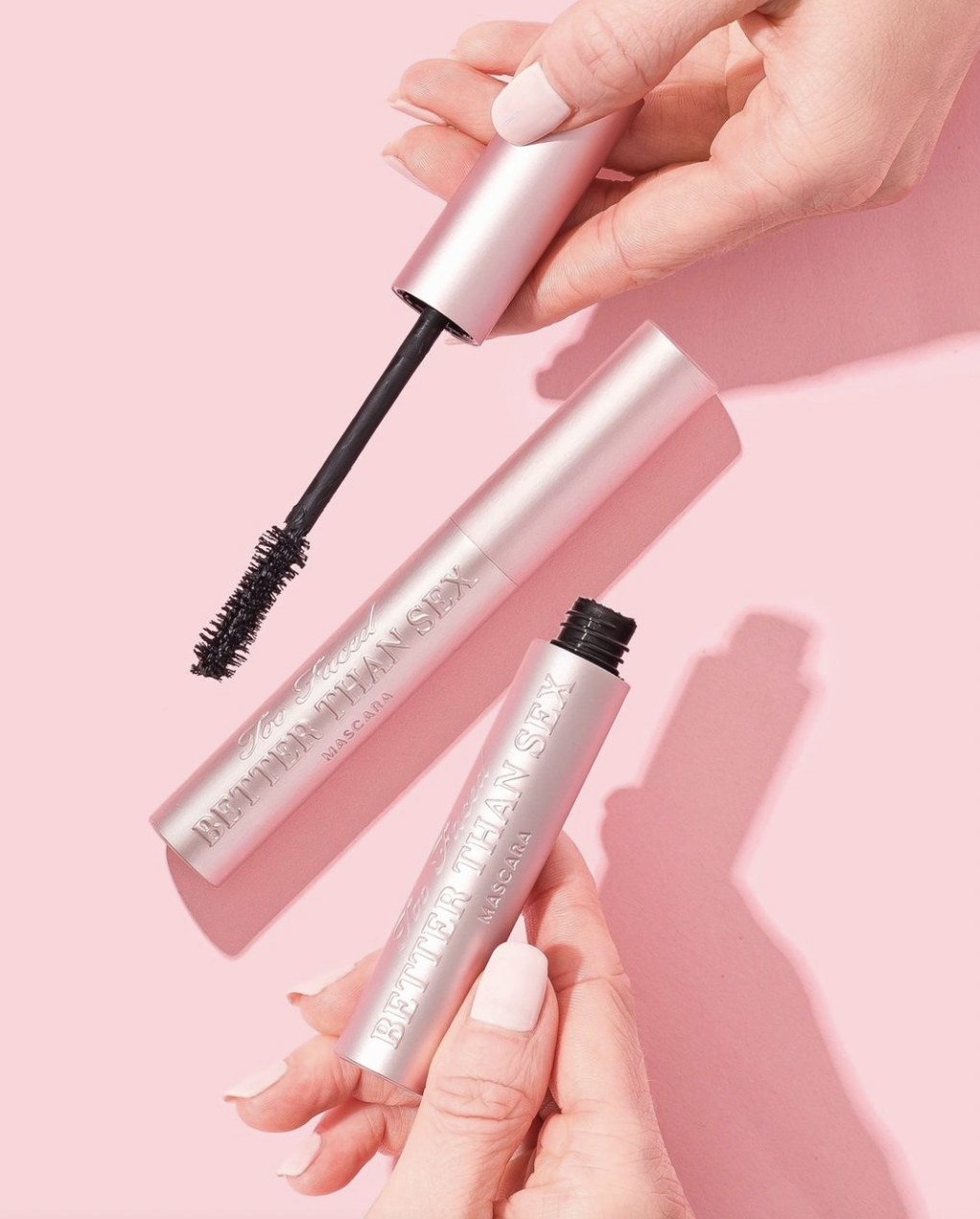A person holding a tube of mascara with another laid in the background