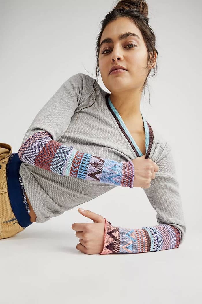 Model wearing the grey long-sleeve with multi-colored patterned designs on cuff from wrist to elbow