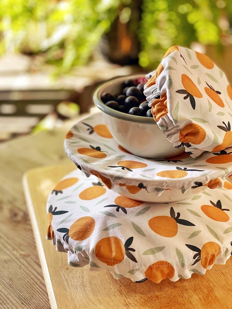 three bowls in different sizes covered by the cotton food covers, which look like shower caps and have cute illustrated oranges on them