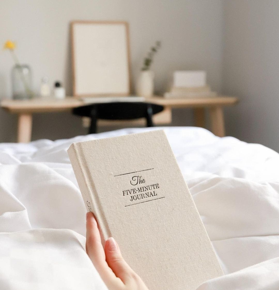 someone holding the five minute journal while lounging in bed