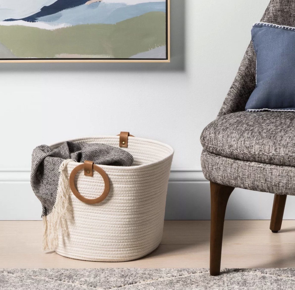 The white coiled basket with brown rounded leather straps is set up in a neutral room