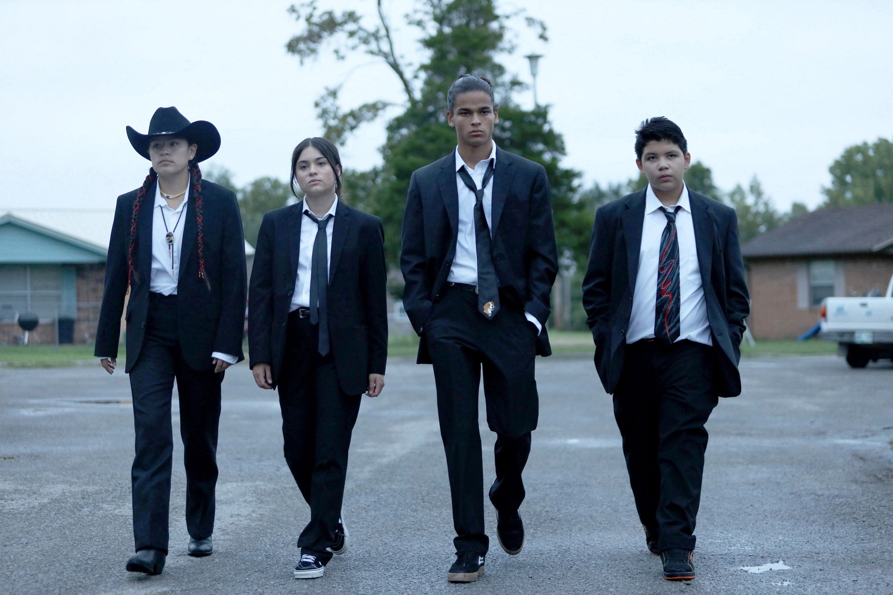 the main cast walking in suits and ties across a parking lot