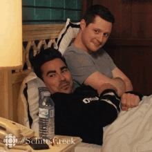 Patrick and David lying in the bed, blushing and smiling