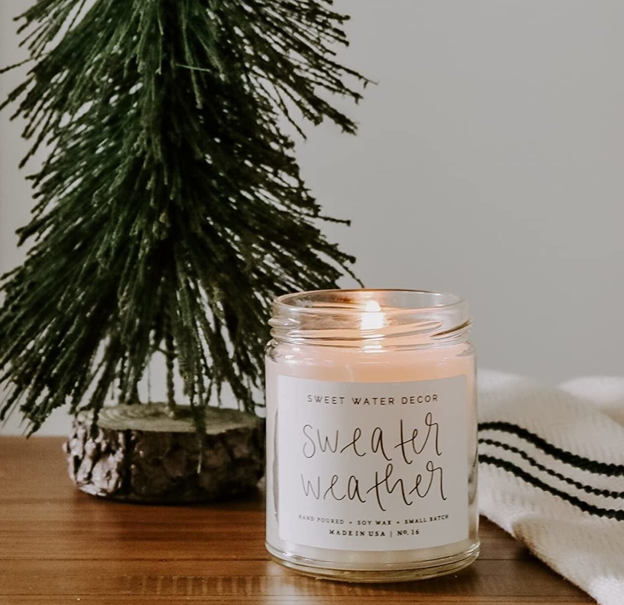 The lit sweater weather candle next to a small decorative tree