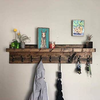 The coat rack being used to hang a jacket, umbrella, and keys, with some plant vases and picture frames displayed on the shelf