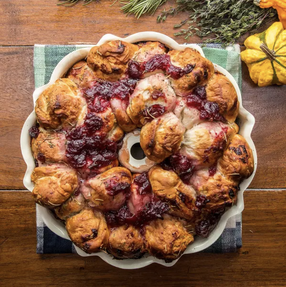 An overhead shot of a fluted tube cake pan with freshly baked pull-apart monkey bread (including biscuits, brie, cranberry sauce, thyme, and rosemary)