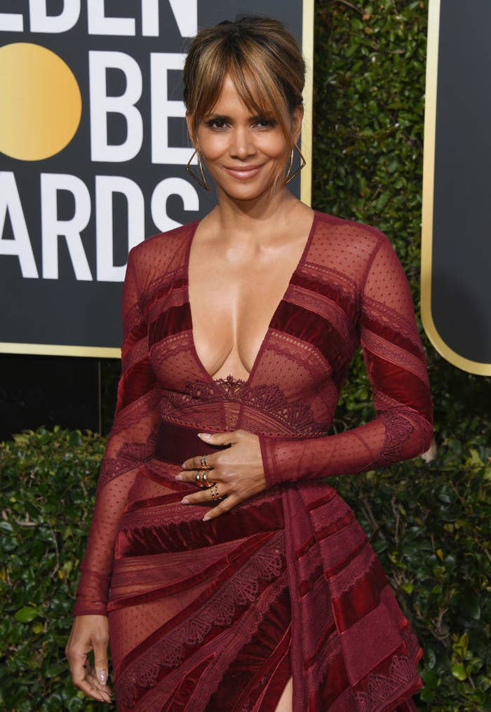 Halle Berry poses on the red carpet in a long-sleeved plunging multi-textured dress and her hair in an updo with bangs