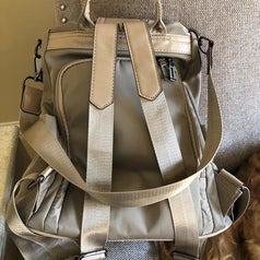 the backview of the gray back showing the main compartment entrance, backpack straps, and a nylon shoulder strap