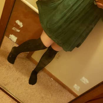 a reviewer wearing a pair of over-the-knee socks with. a green dress