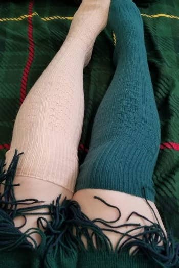 a reviewer wearing a green over-the-knee sock on one leg, and a pink over-the-knee sock on the other