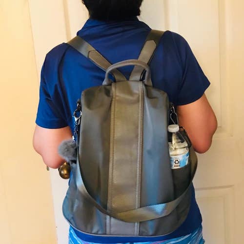 a reviewer wearing the backpack in black with a water bottle in one of the side pockets