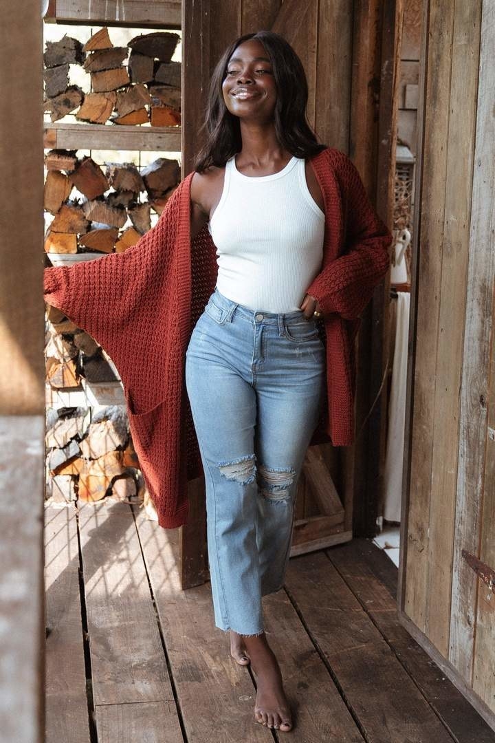 a model in jeans, a white tank, and an oversized orange knit cardigan