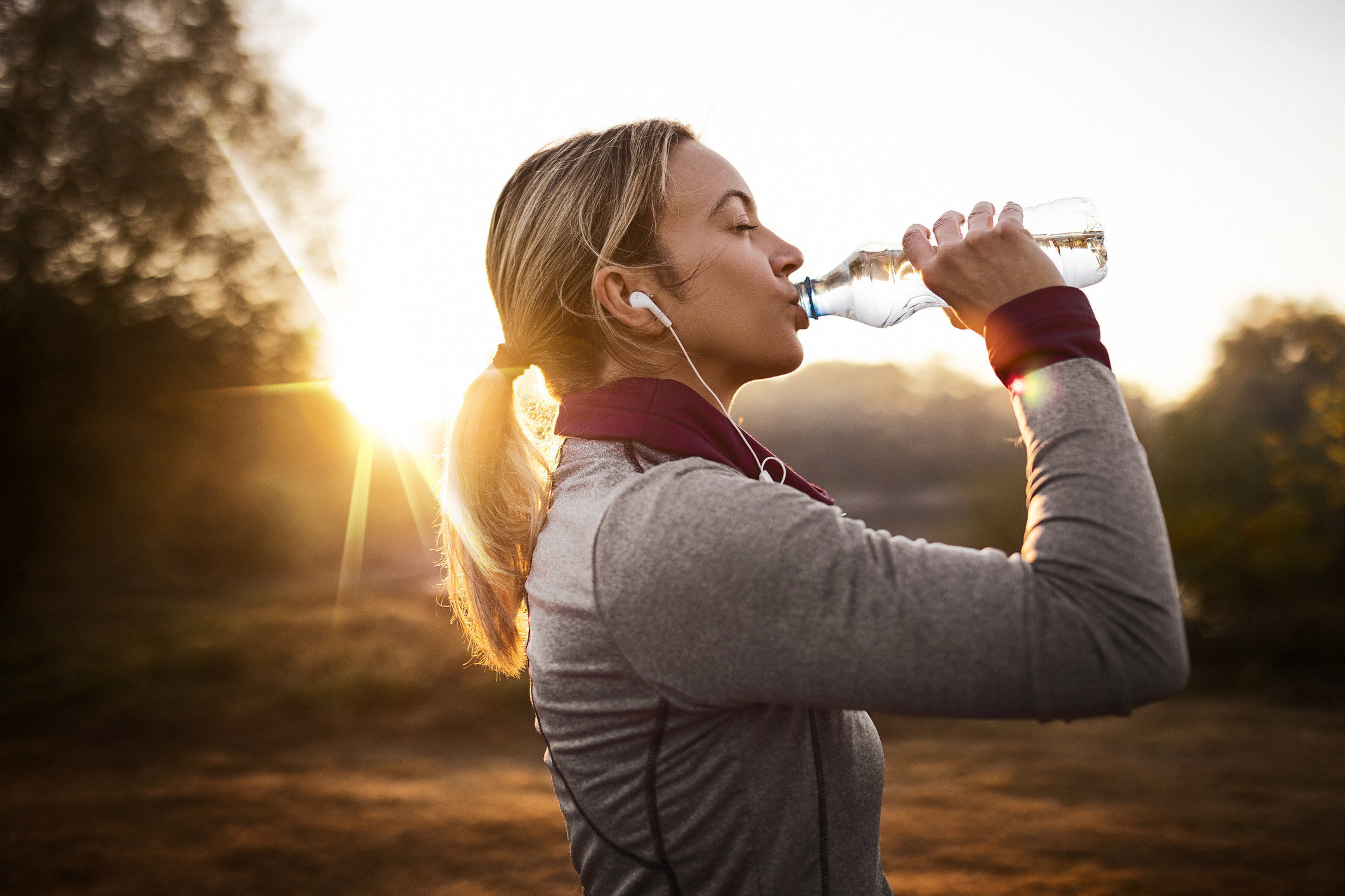 Young woman taking a water break from jogging in nature during sunrise