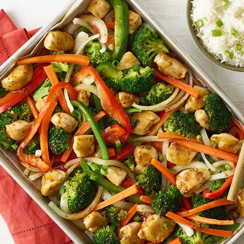 baking sheet filled with broccoli, bell peppers, carrots, and chicken breast served with a bowl of rice