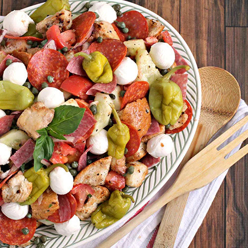 large serving bowl of salad with mozzarella pearls, pepperoni, tomatoes, and bread cubes