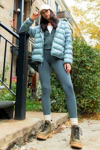 a model wearing leggings and a puffer jacket with the lace-up boots in khaki green with a tan lug sole