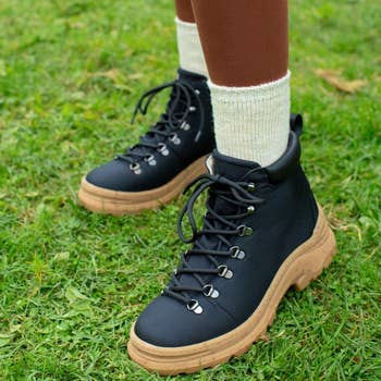 a close-up of a model wearing black lace-up boots with a tan lug sole