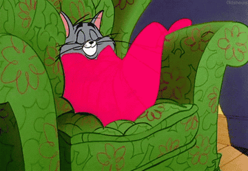 a gif of Tom from tom and jerry curling up in a blanket on the couch