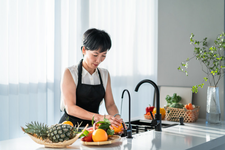 A person wearing an apron washing fruit at the kitchen sink