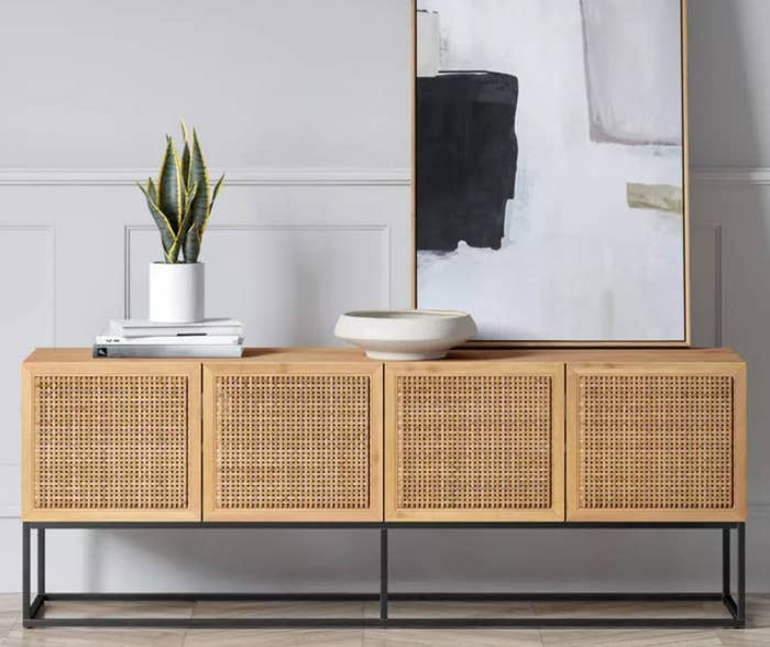 A woven 4-door TV stand with black metal legs. It has a soft neutral solid wood finish which can easily blend with any home decor.