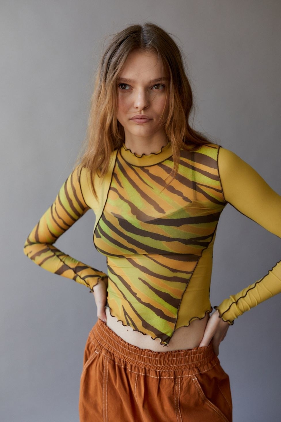 model in mesh yellow, green, orange, and brown patterned long sleeve shirt