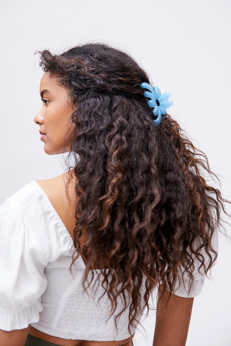 model with the front pieces of thier curly hair pulled back in a blue butterfly claw clip
