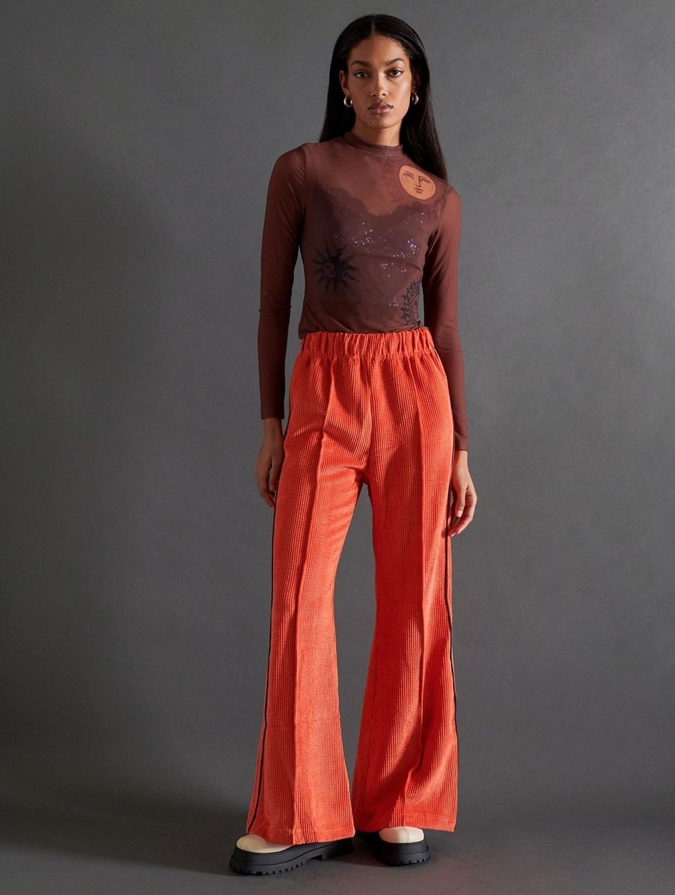 model in orange corduroy wide-legged pants with an elastic waist and seams down the front of the legs