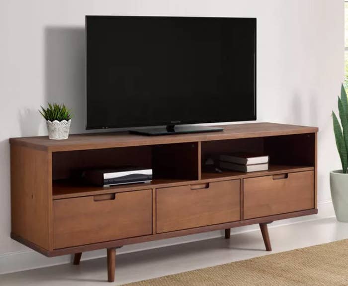A dark brown wooden finish TV stand with 3 pull out drawers and 2 open cubbies. Stands on 4 wooden legs and can hold up to a 65&#x27; TV.