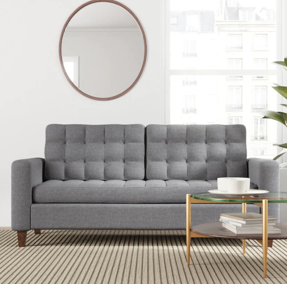 A grey upholstered sofa with square arms and wooden legs