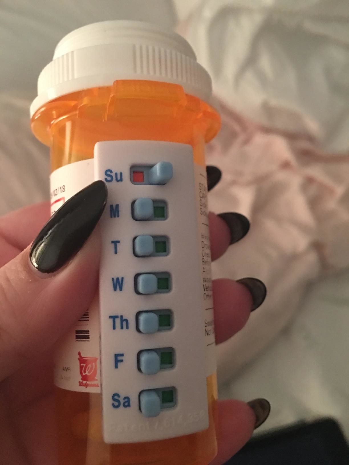 reviewer holding pharmacy pill bottle with device stuck on that has a yes/no slider for each day of the week