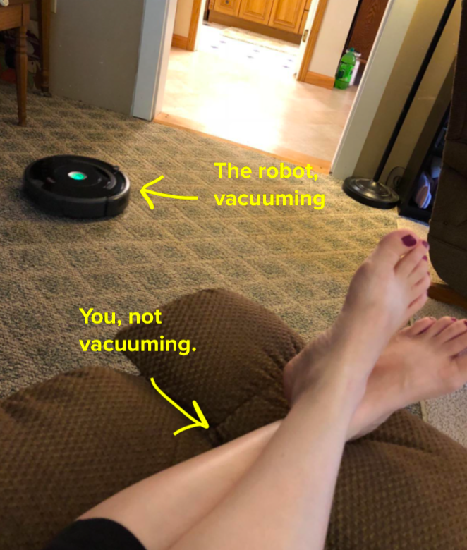 reviewer&#x27;s feet kicked up on the chair while the roomba robot vacuums the room floor