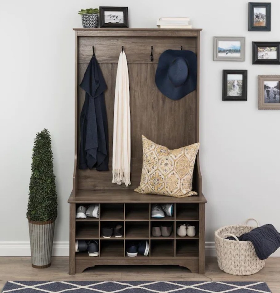 A drifted grey wooden hall tree with four hooks, a bench, and 15 cubbies