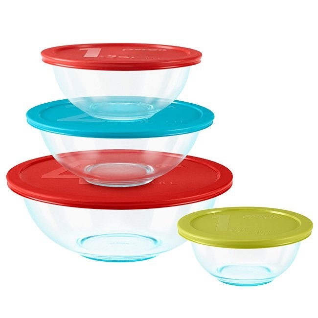 Three glass mixing bowls of varying sizes along with their lids are stacked on top of each other. The fourth mixing bowl, the smallest, sits just to the right