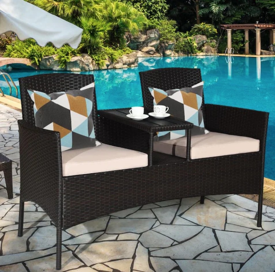 A black rattan outdoor loveseat with a table in the center and cream cushions