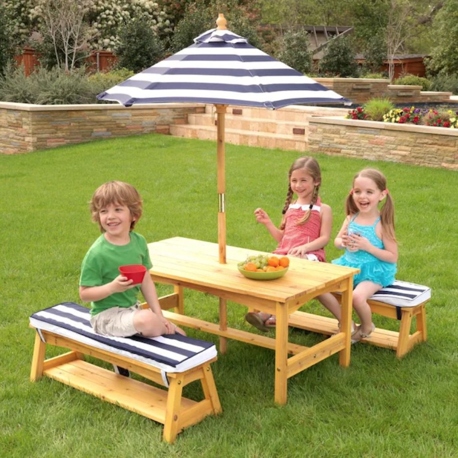 Kids sitting at a kids picnic table with blue/white striped cushions and a matching umbrella in center of table