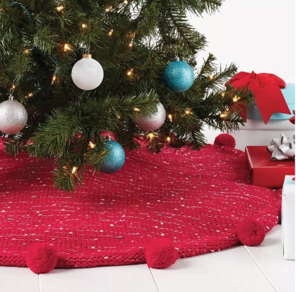 Red tree skirt with red poms on border underneath christmas tree