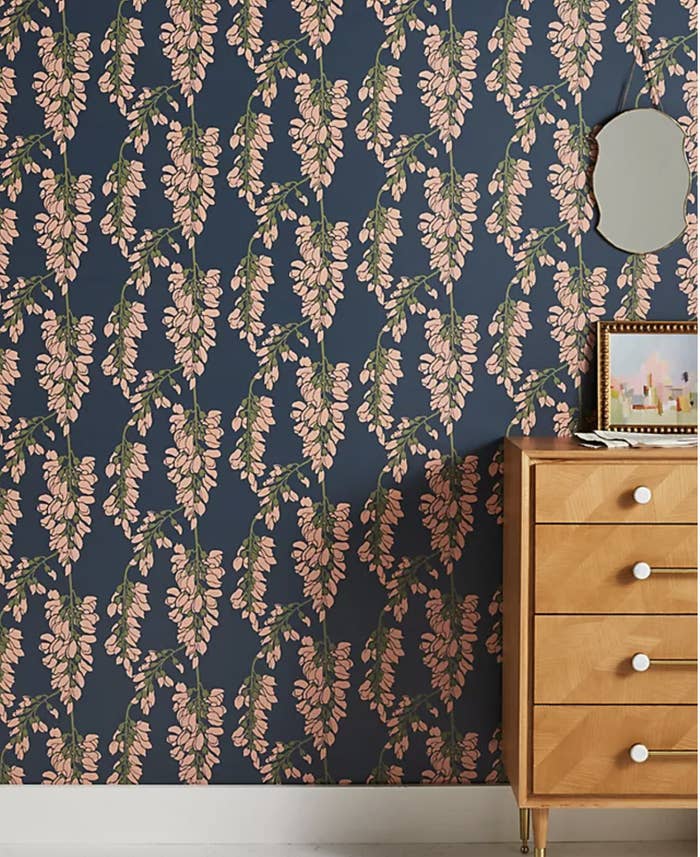 Wooden dresser in front of navy blue, pink, and green floral wallpaper