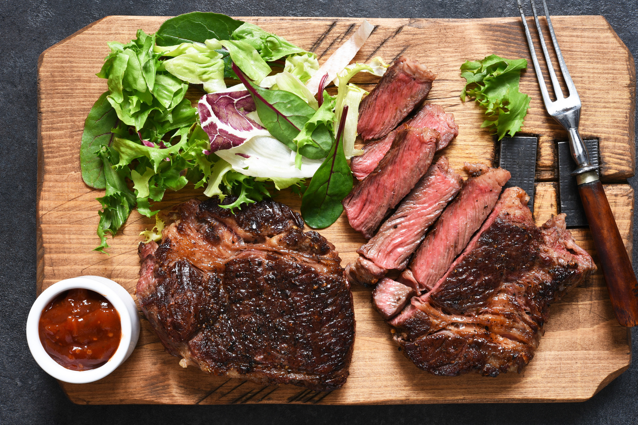 Steak with ketchup on a cutting board.