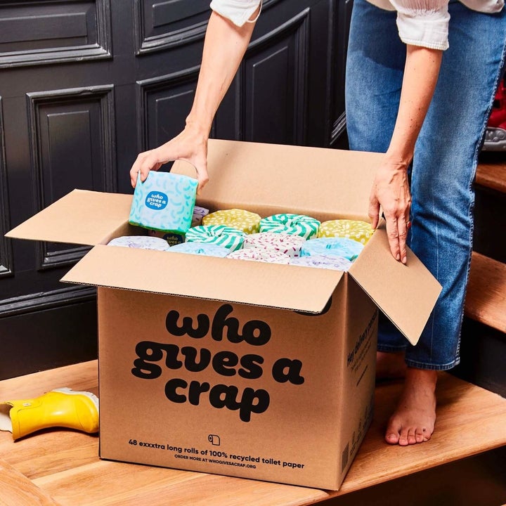 a model pulling a roll of toilet paper out of a box filled with toilet paper that says "who gives a crap"