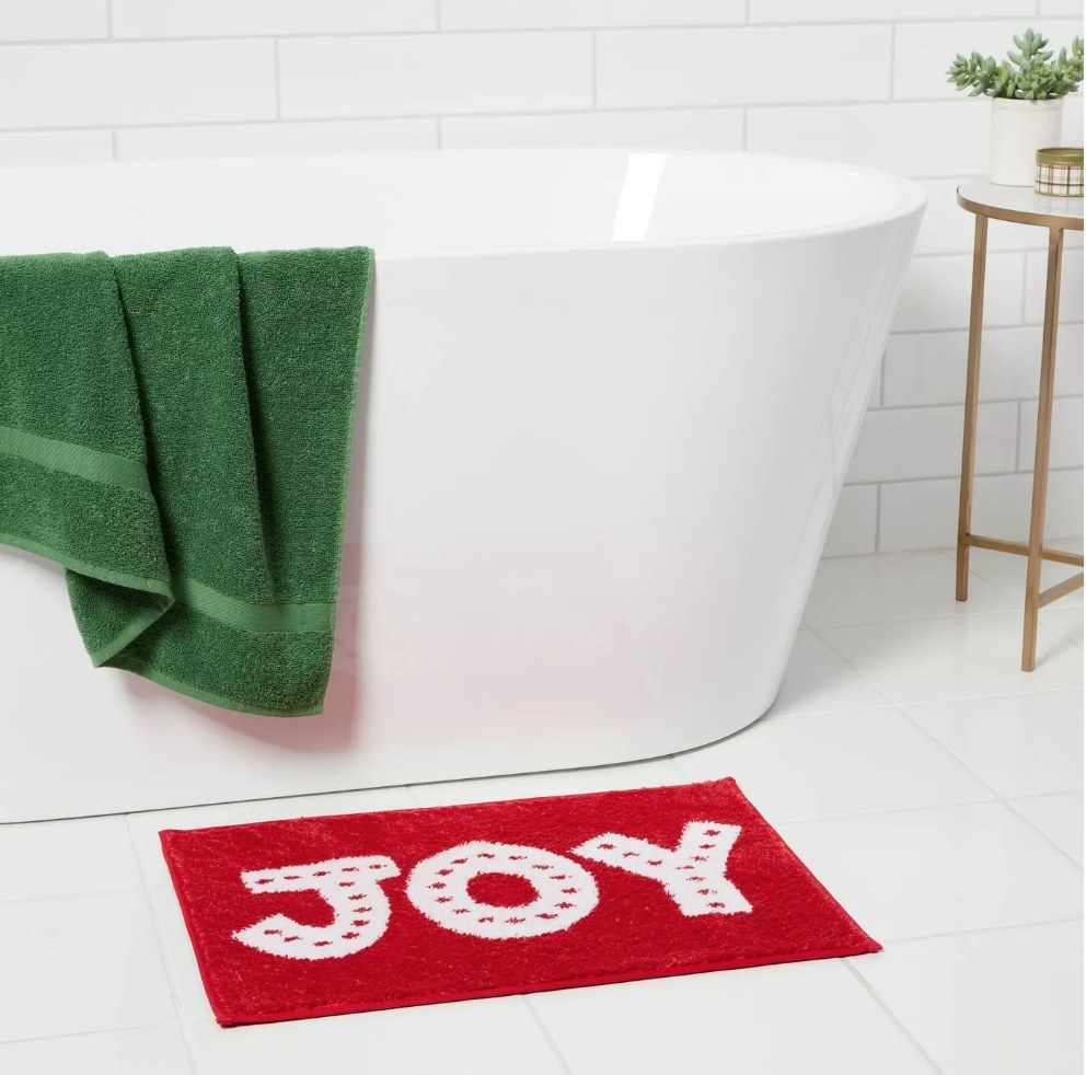 Red bath mat with &quot;Joy&quot; in white letters under white tub