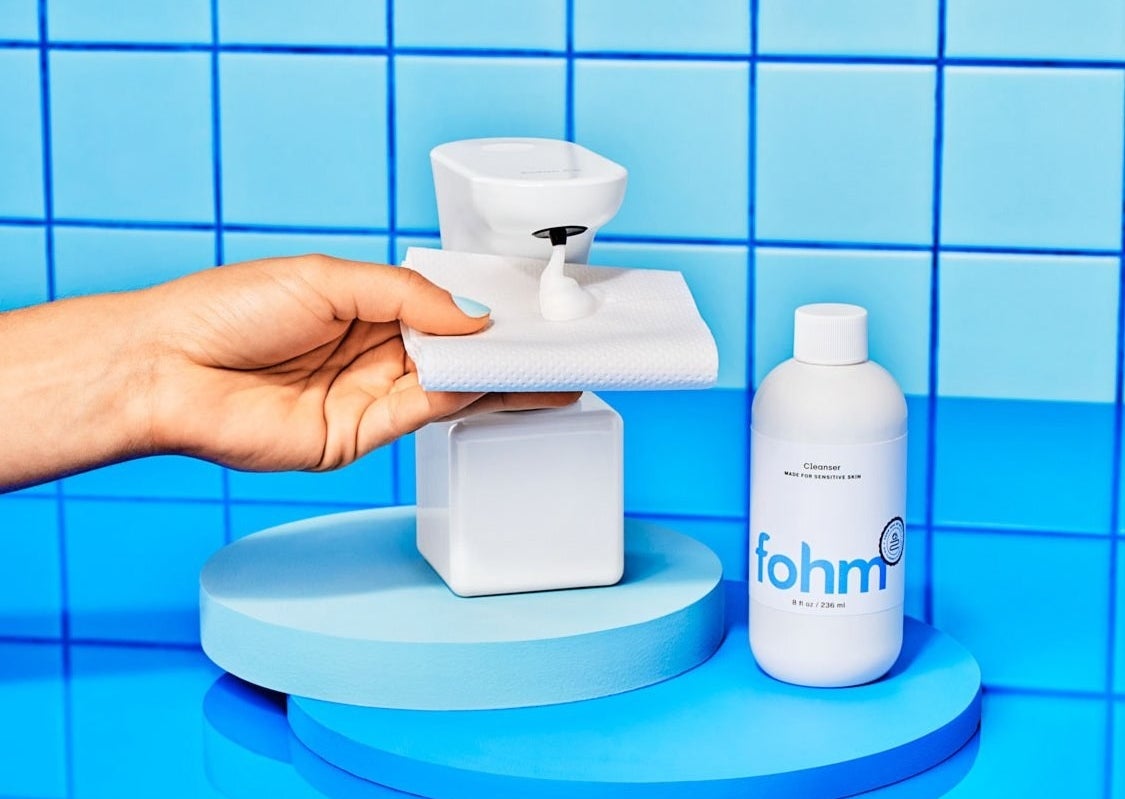 a model placing a piece oof toilet paper under the touchless dispenser next to a refill bottle of foam