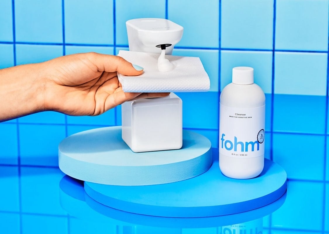 a model placing a piece oof toilet paper under the touchless dispenser next to a refill bottle of foam