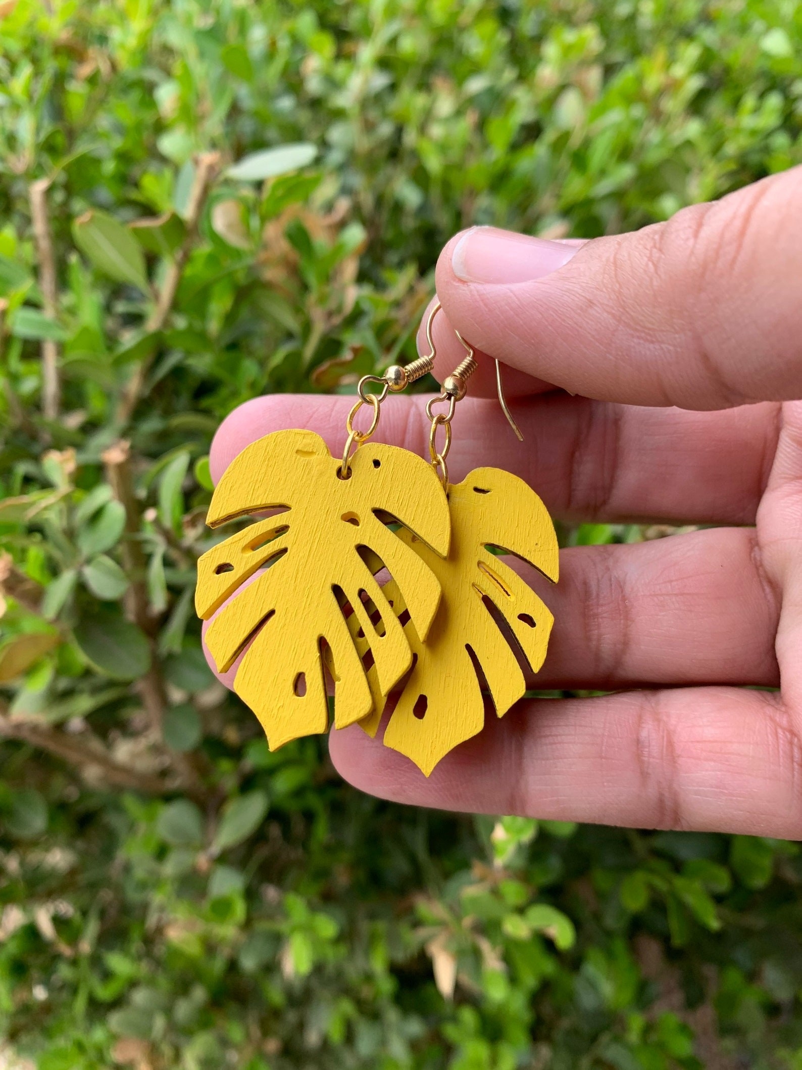 Model holding yellow monstera leaf earrings in hand