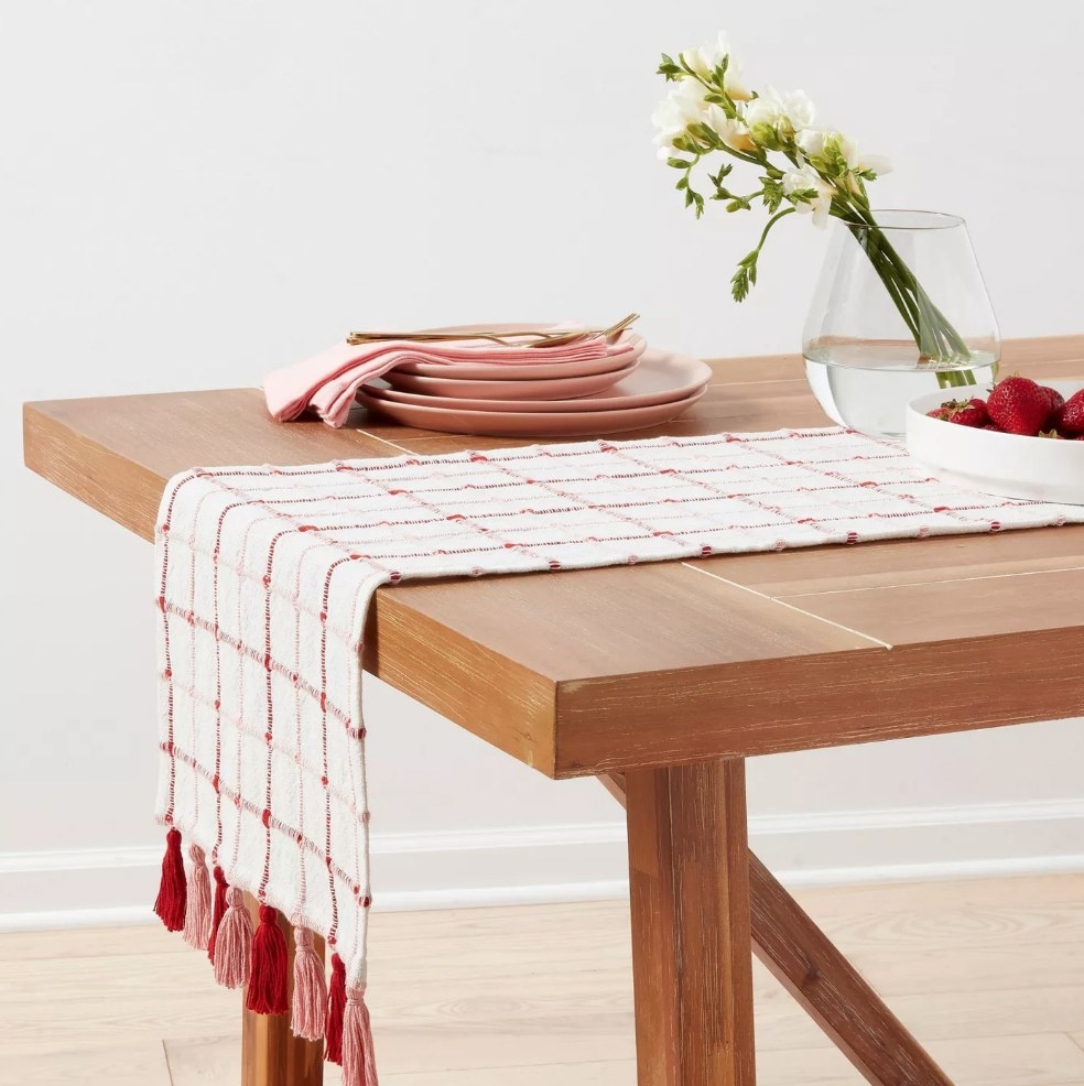 White table runner with red checker design and red/pink tassles on wooden table