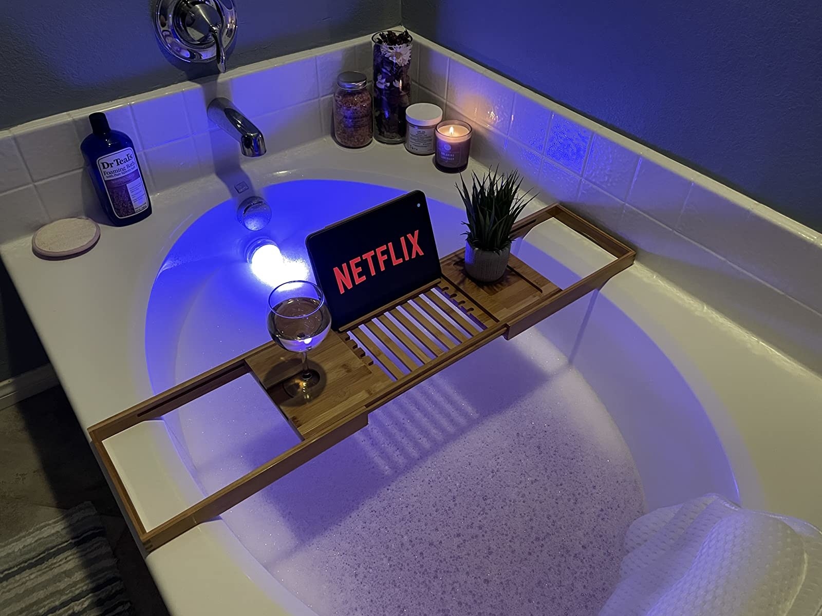same expandable bath caddy in tub with filled wine glass and tablet that has Netflix on the screen
