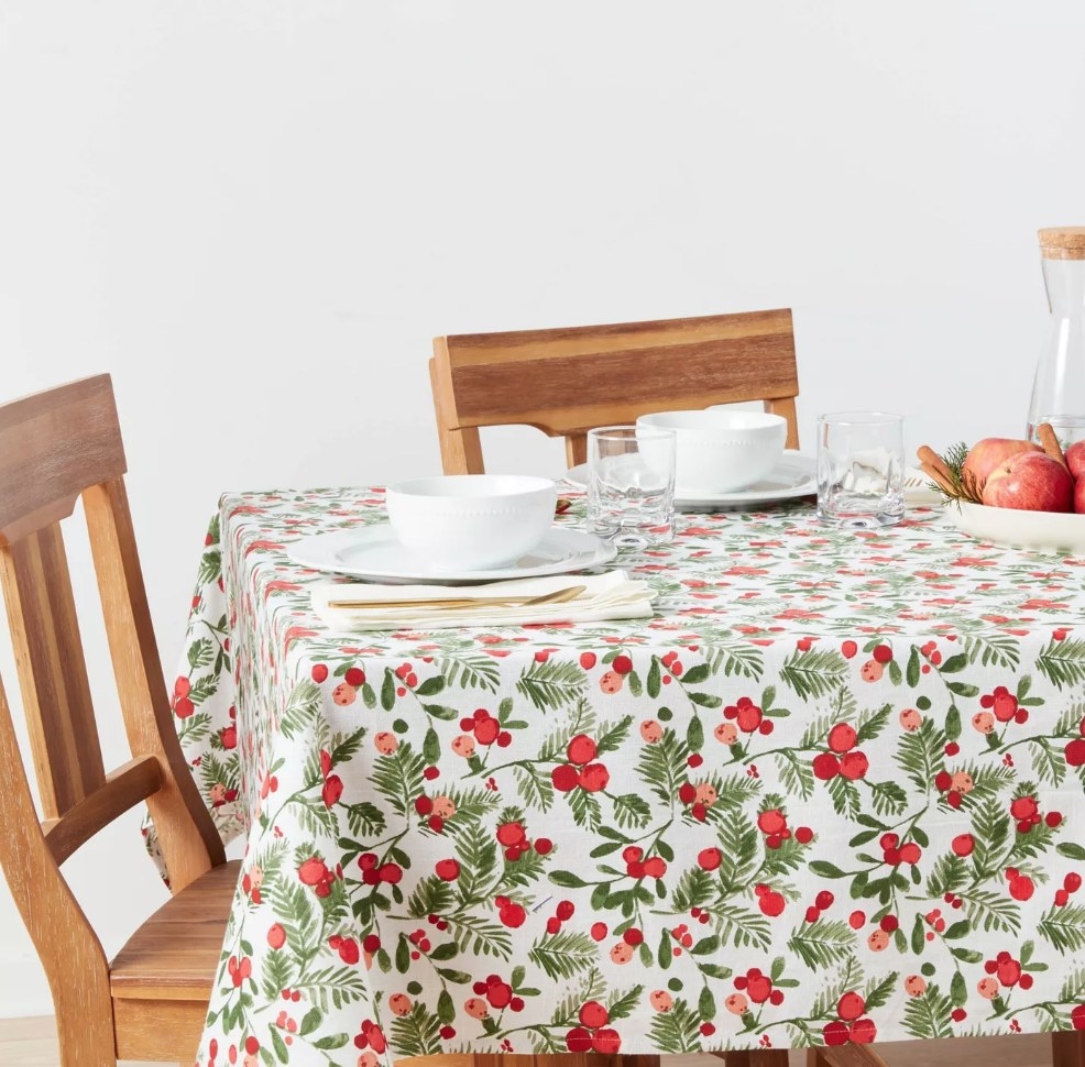 Holly berry red, green and white table cloth, wooden chairs, white plates and glasses on top of table